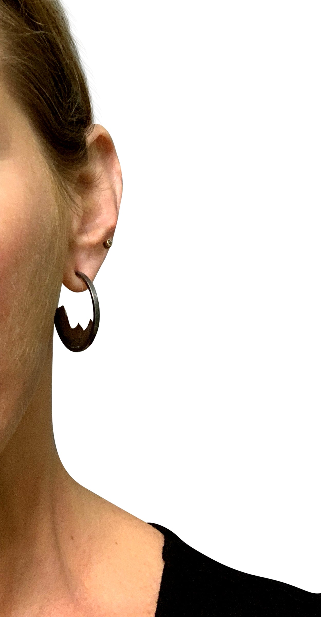 A woman's left ear, facing the camera, wearing an open-hoop earring. Nestled into the bottom half of the hoop is a textured ombre silver piece, like a slice of a mountain range. The bottom of the earring hangs down about halfway between her nose and upper lip.