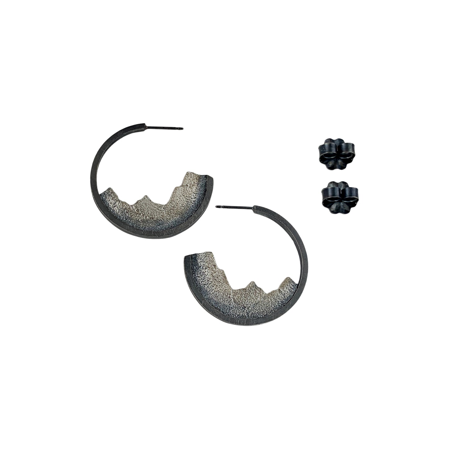 A vertical view of two open-hoop earrings with silver posts. Nestled into the bottom halves are textured ombre silver pieces, like slices of a mountain range. Two fasteners are shown to the side.
