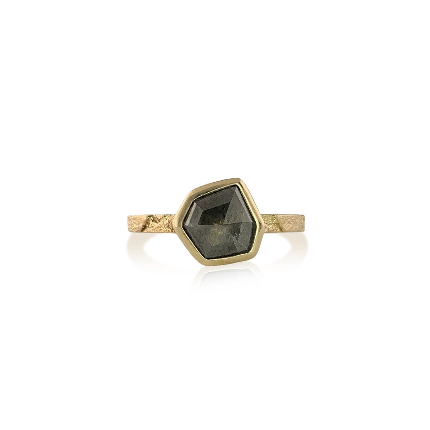Front view of a ring with a narrow, textured gold band. At the center is a gray speckled six-irregular-sided diamond.The diamond is encased in a smooth gold wrapping.