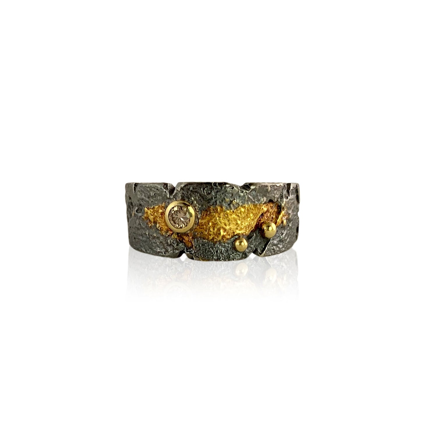 Front view of a wide, textured dark gray band with a swish of gold in the middle. A gold-wrapped diamond sits to the left, and to the right are two gold balls.
