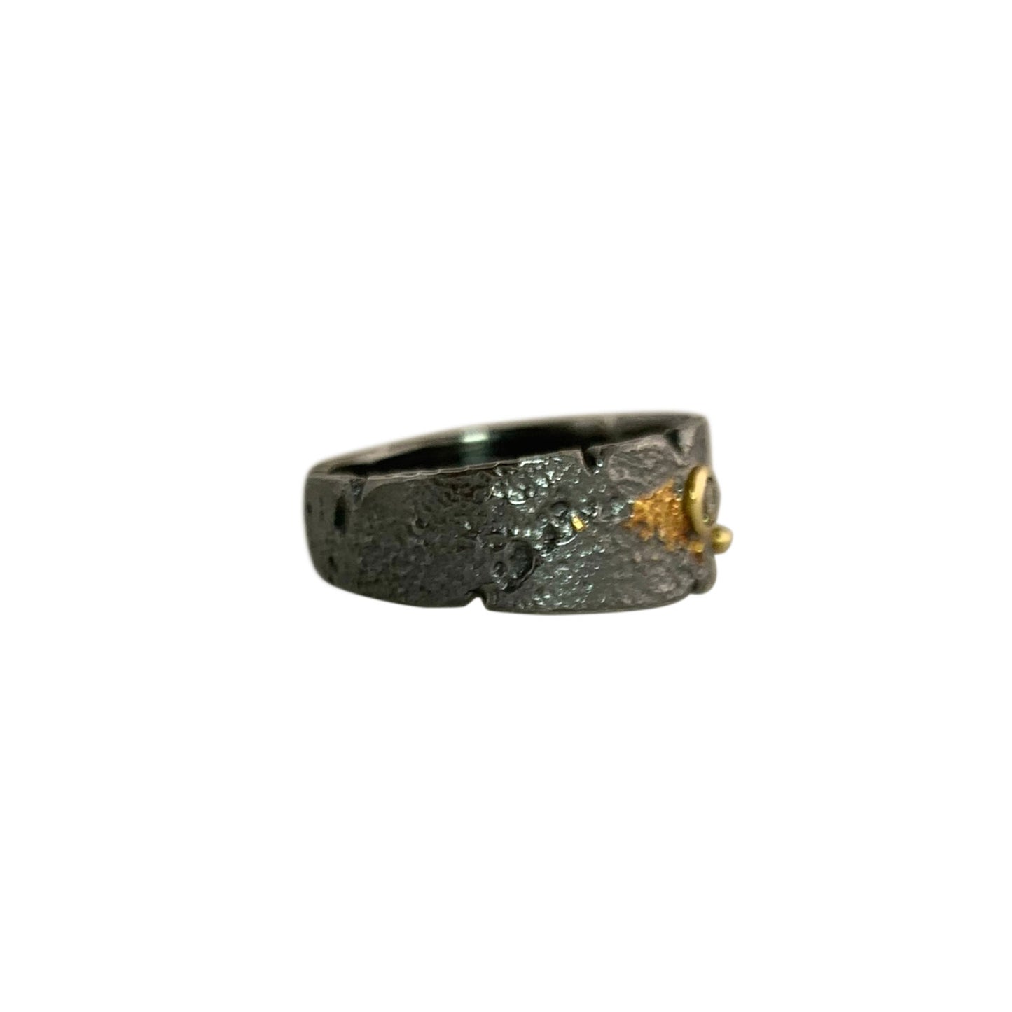 Side view of a textured dark gray band that is narrower on the left and wider on the right. On the right, there's a side/front view of a gold-wrapped diamond and a small gold ball.
